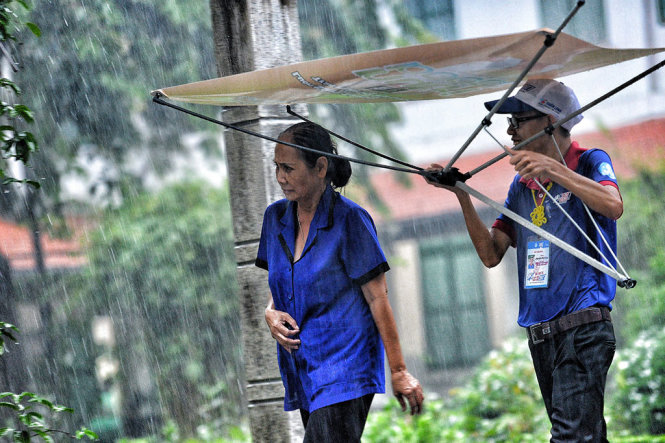 Sinh viên tình nguyện dùng tạm miếng logo tiếp sức đến trường che mưa cho phụ huynh đi đón con - Ảnh: HỮU KHOA